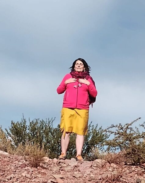 Denise, está vestida de rojo y amarillo, mirando hacia la montaña, al fondo se ve el cielo azul